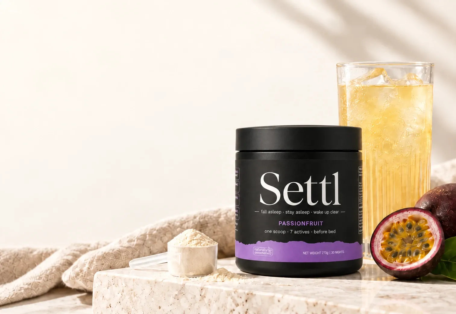 A Settl tub, a glass of the drink, the scoop and a halved passionfruit on a stone bench