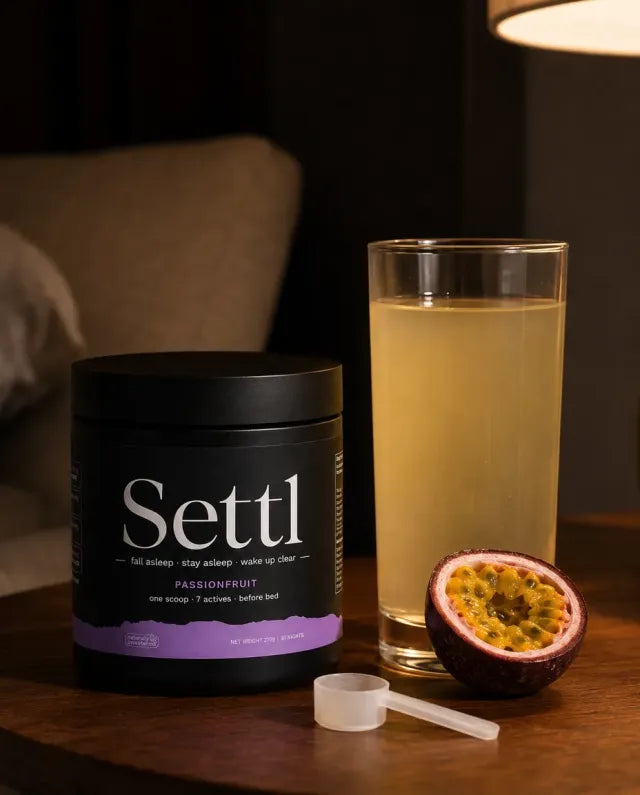 A tub of Settl and a full glass of cold water on a bedside table under a warm lamp.