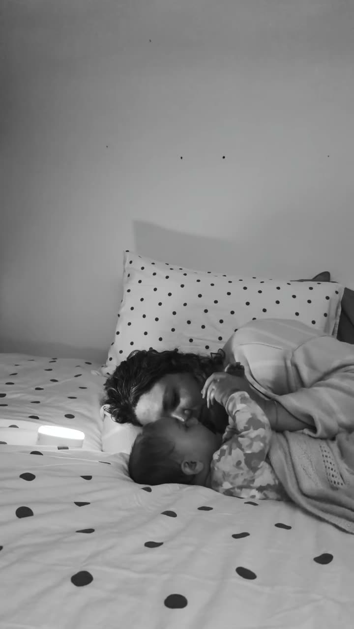 Sarah asleep on a bed beside her baby with a small night light on the sheet, in black and white.