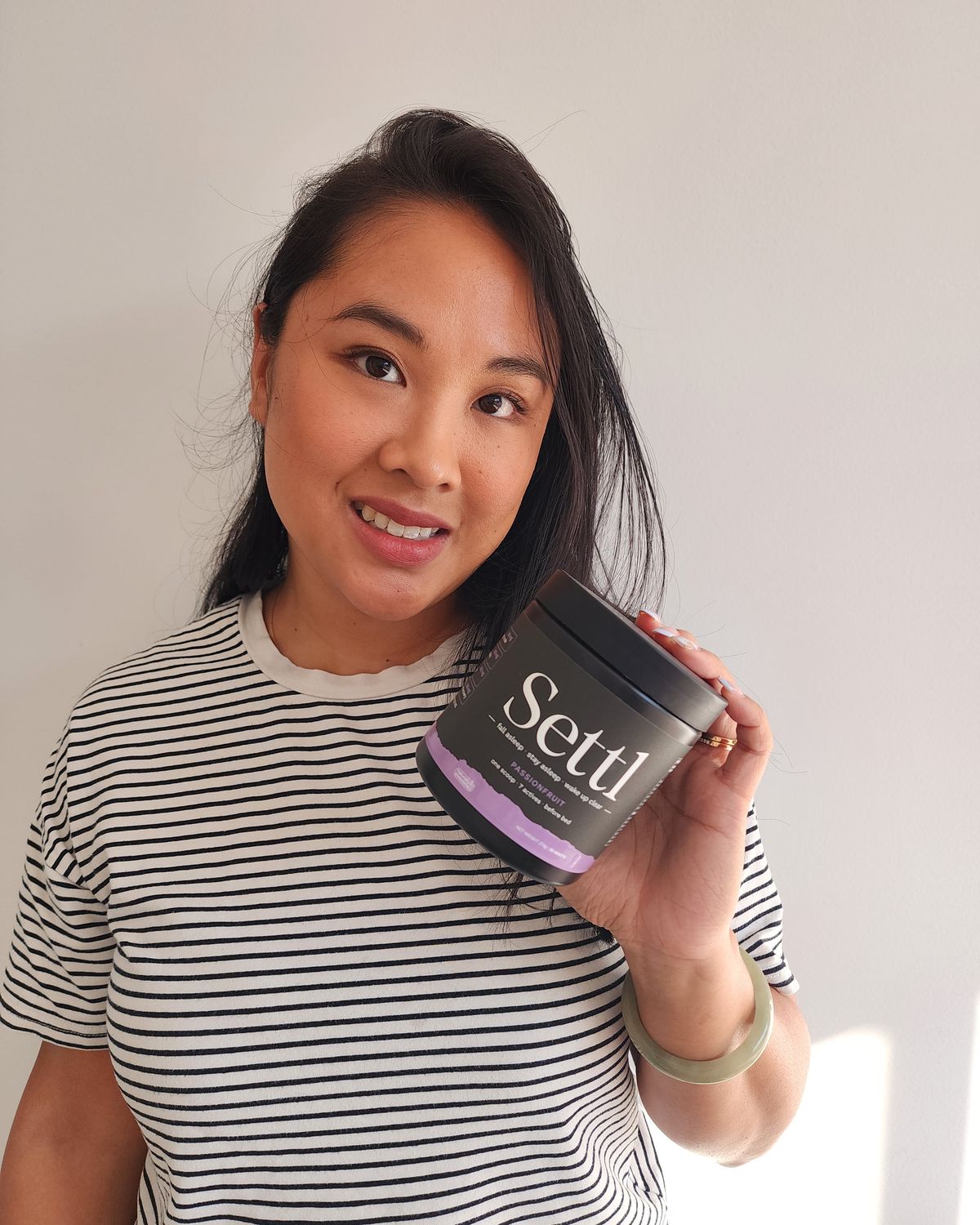 Veronica smiling and holding a tub of Settl Passionfruit against a white wall.